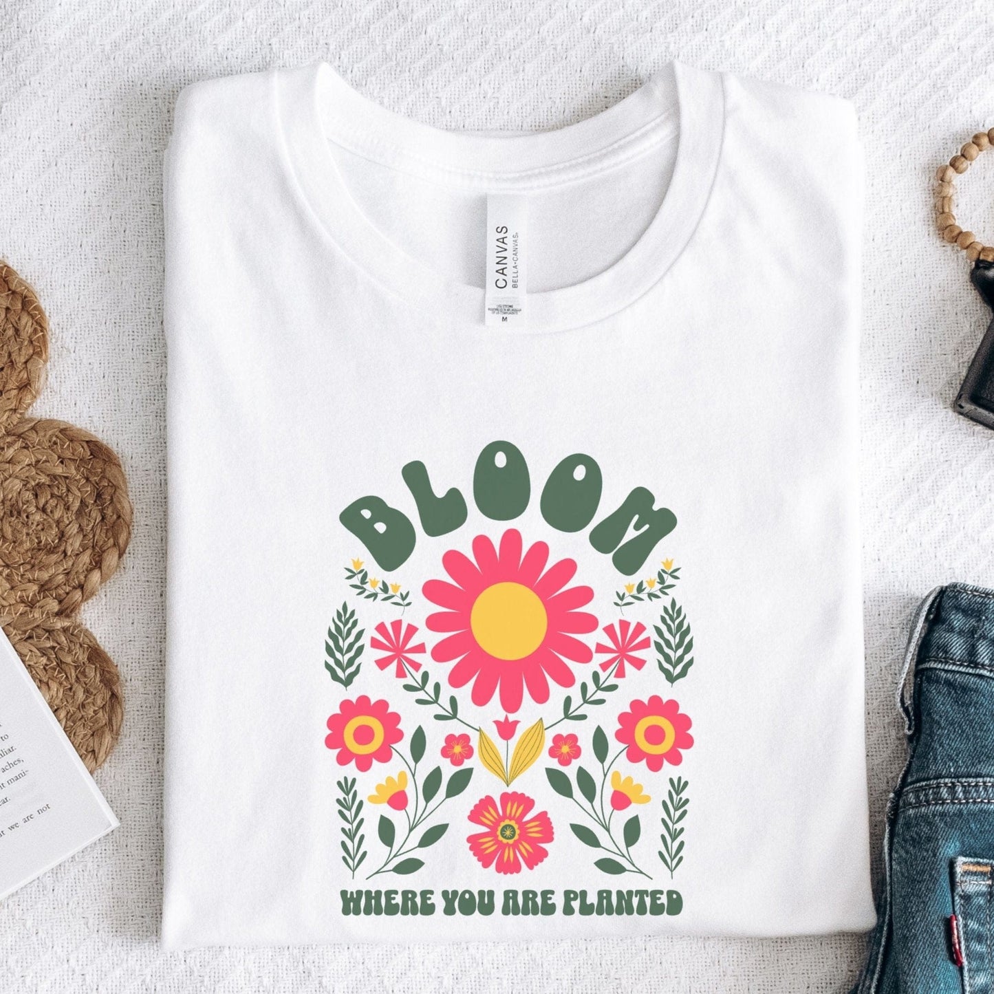 “Bloom Where You Are Planted” t-shirt with bold retro florals and uplifting message in green, pink, and yellow tones.