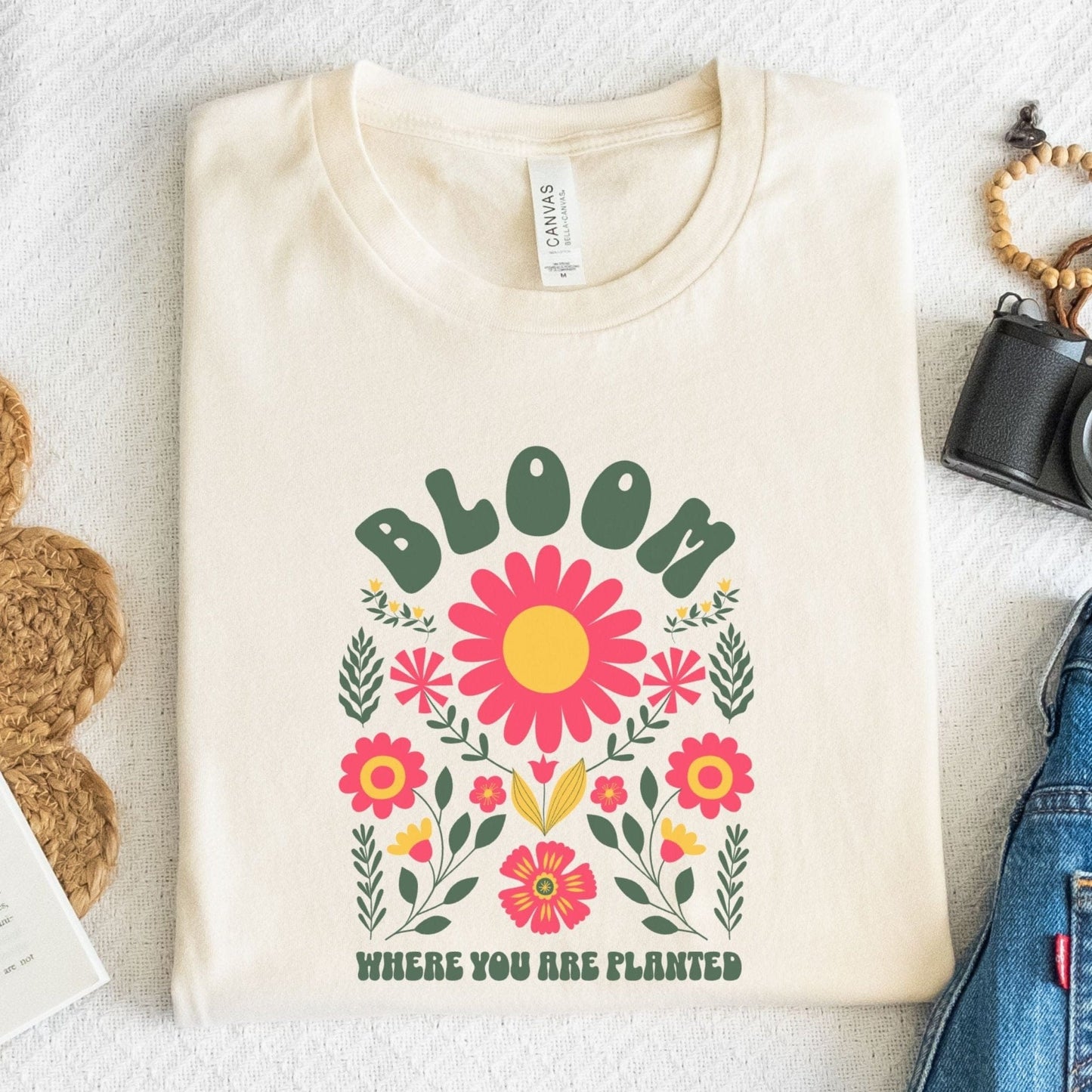 “Bloom Where You Are Planted” t-shirt with bold retro florals and uplifting message in green, pink, and yellow tones.