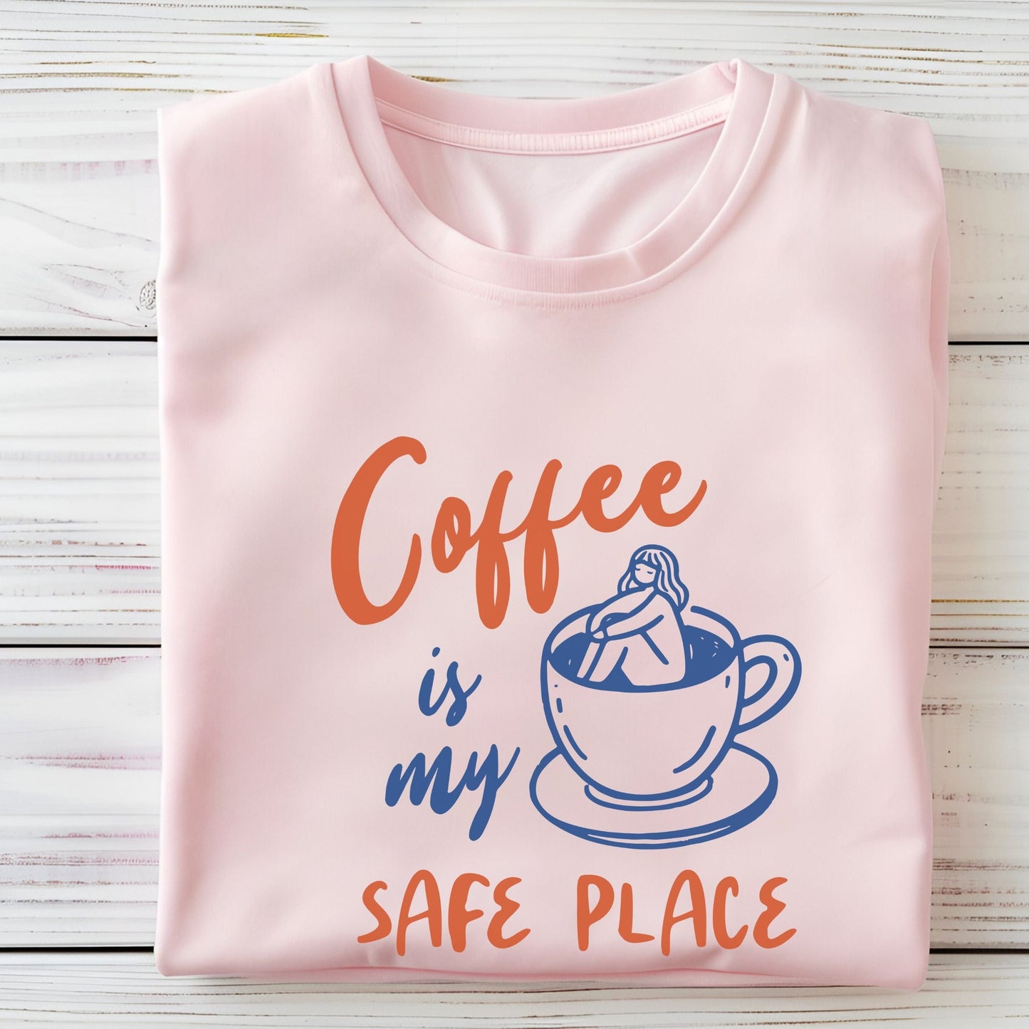 Blue and orange graphic t-shirt with text “Coffee is my safe place” featuring a girl sitting inside a coffee cup illustration.