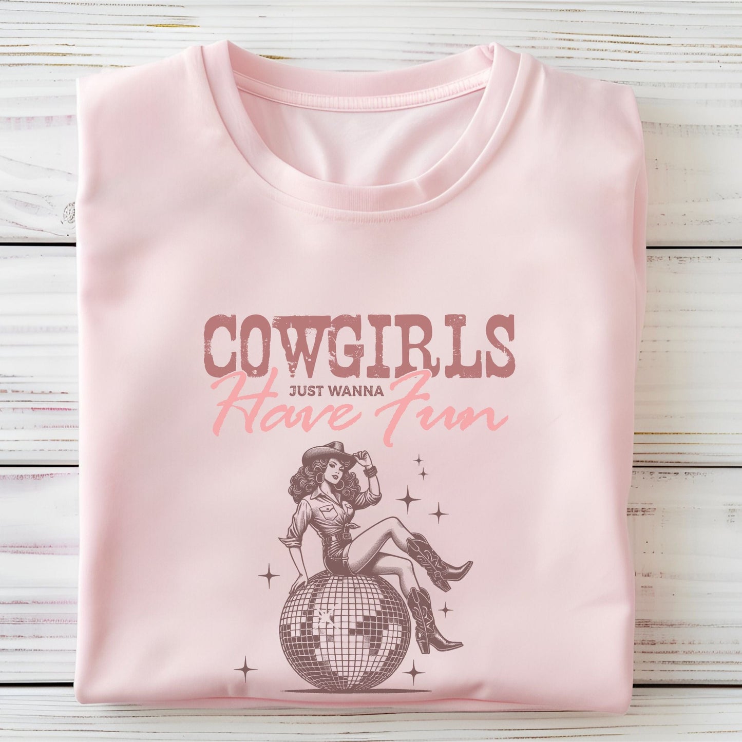 T-shirt featuring retro cowgirl design with “Cowgirls Just Wanna Have Fun” text in pink