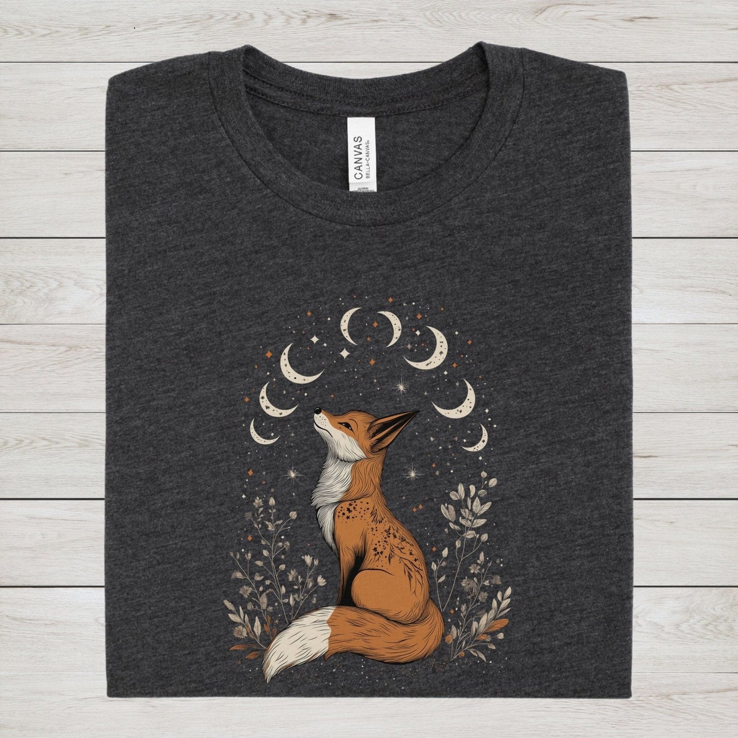 Celestial fox t-shirt with a woodland fox sitting under moon phases, surrounded by stars and hand-drawn floral illustrations in neutral tones.
