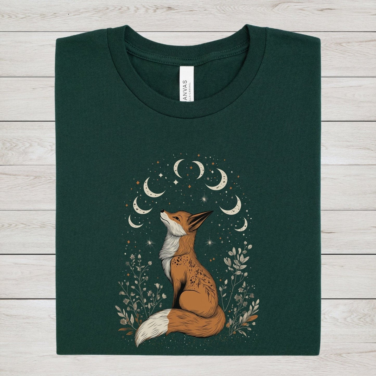Celestial fox t-shirt with a woodland fox sitting under moon phases, surrounded by stars and hand-drawn floral illustrations in neutral tones.