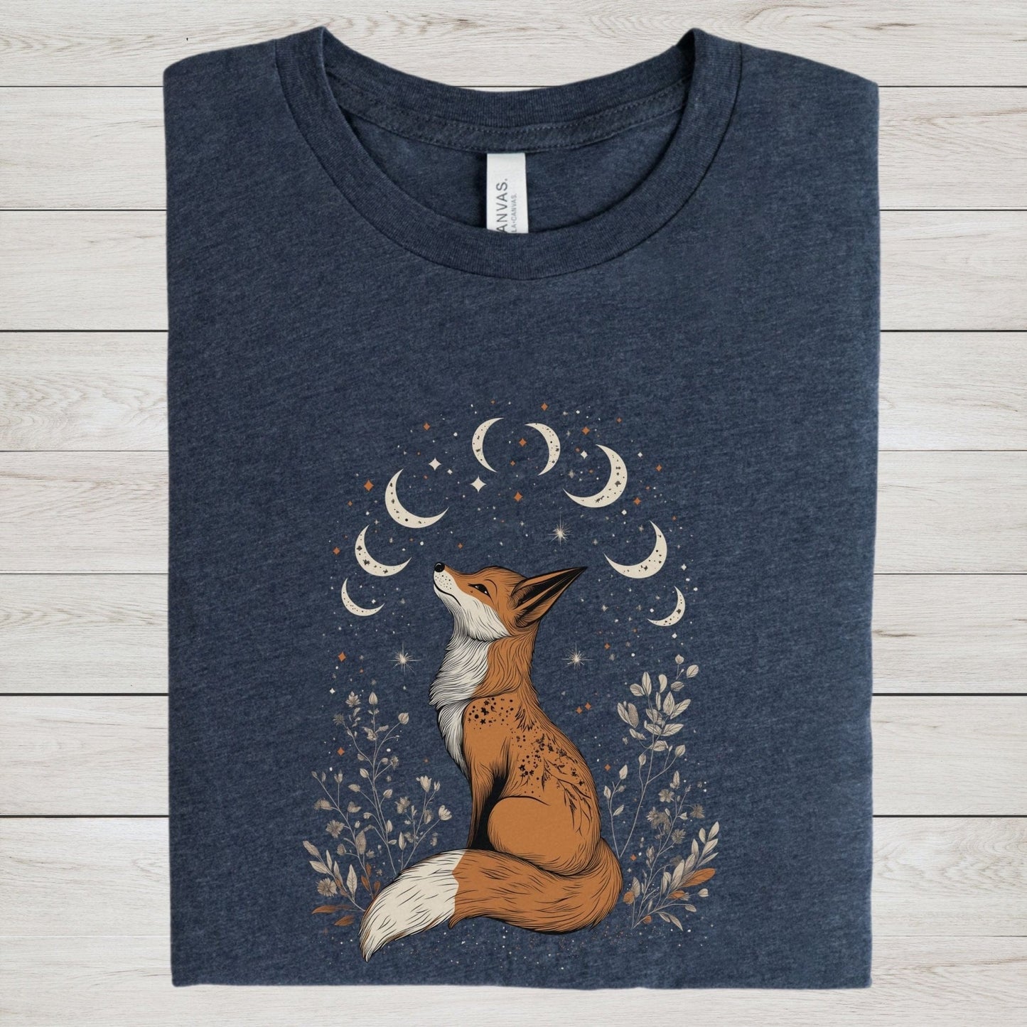 Celestial fox t-shirt with a woodland fox sitting under moon phases, surrounded by stars and hand-drawn floral illustrations in neutral tones.