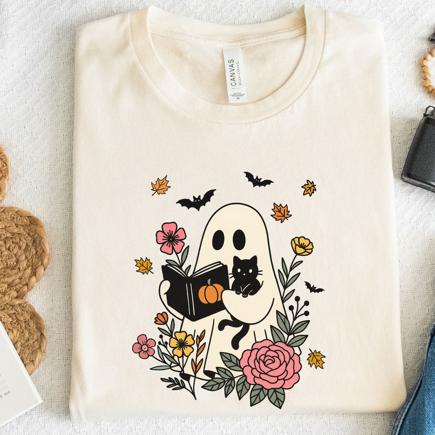 Natural t-shirt with a ghost reading a book and a black cat design, surrounded by flowers and leaves.