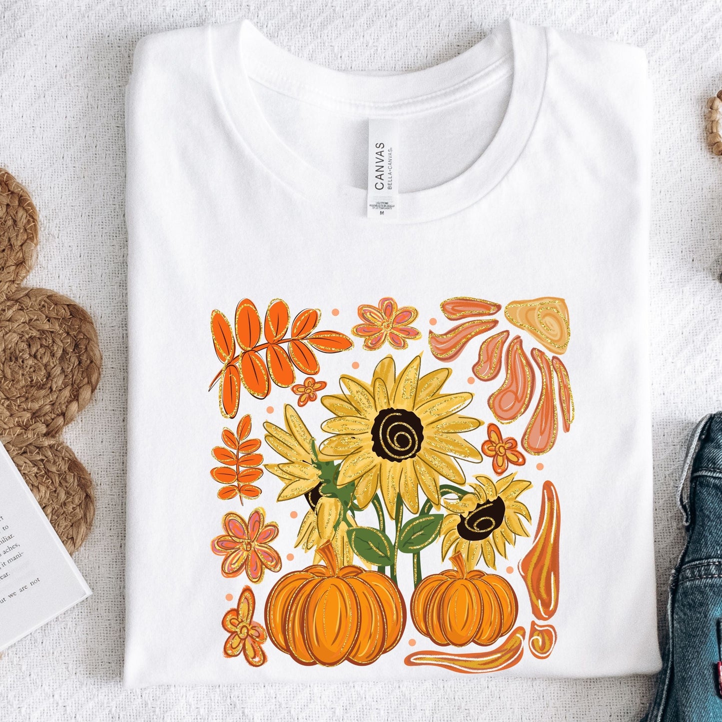 White t-shirt with autumn-themed design featuring sunflowers and pumpkins on a textured surface.