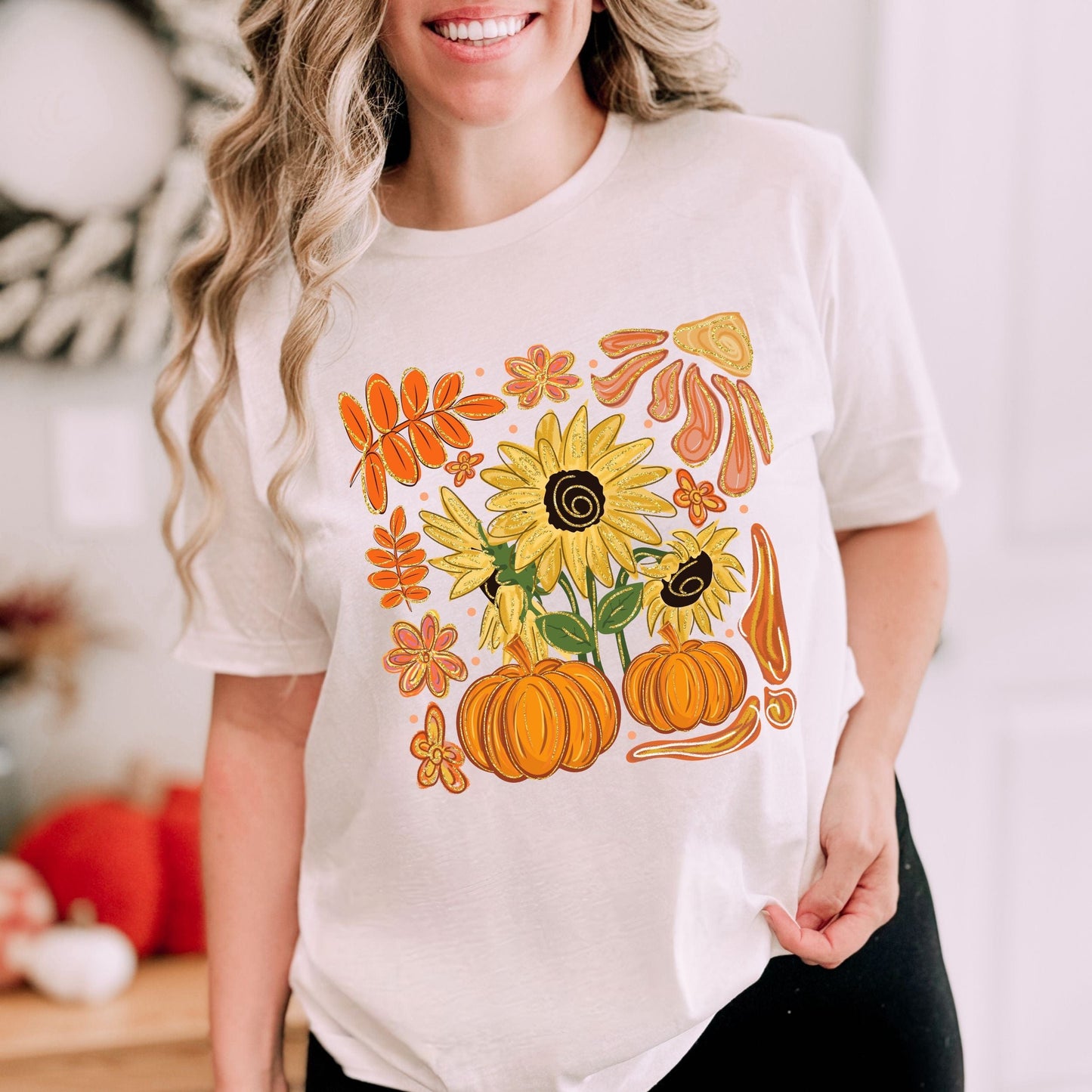 Person wearing a white t-shirt with autumn-themed design featuring sunflowers and pumpkins.