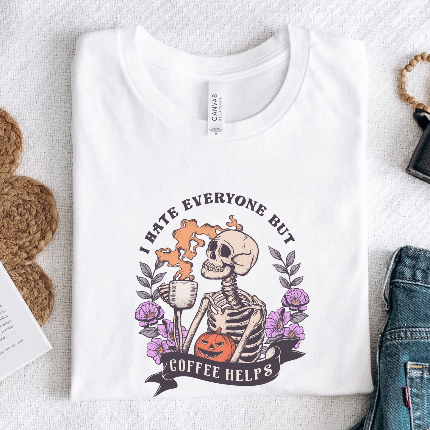 “I Hate Everyone But Coffee Helps” t-shirt with skeleton drinking coffee, purple flowers, jack-o’-lantern, and gothic Halloween design.