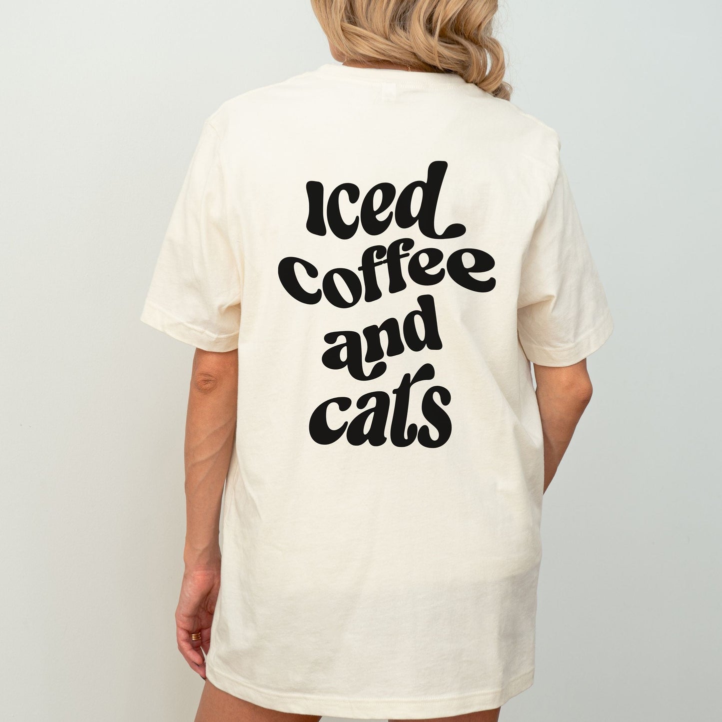 T-shirt with “Iced Coffee and Cats” in bold lettering, modeled in a cozy indoor setting.