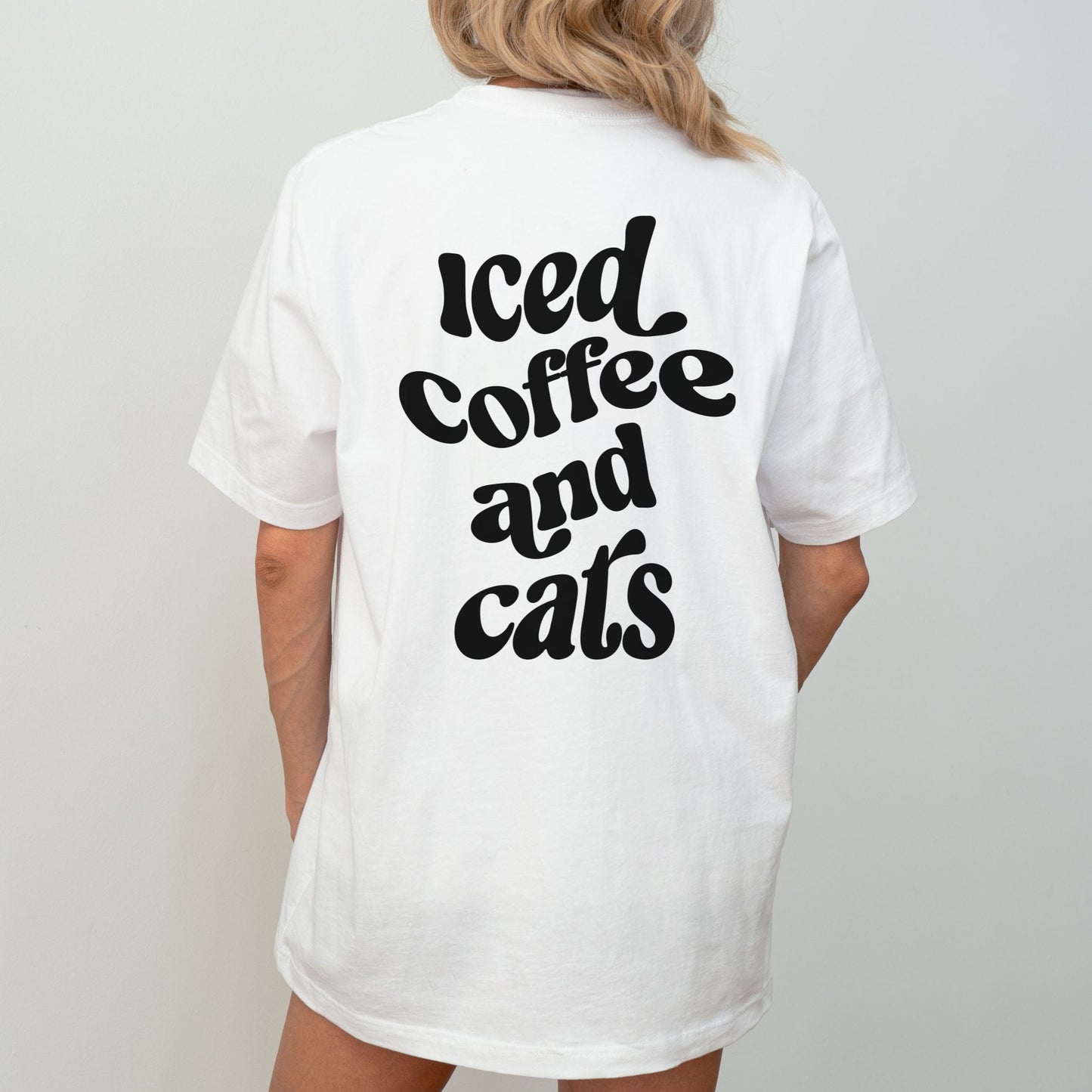 T-shirt with “Iced Coffee and Cats” in bold lettering, modeled in a cozy indoor setting.