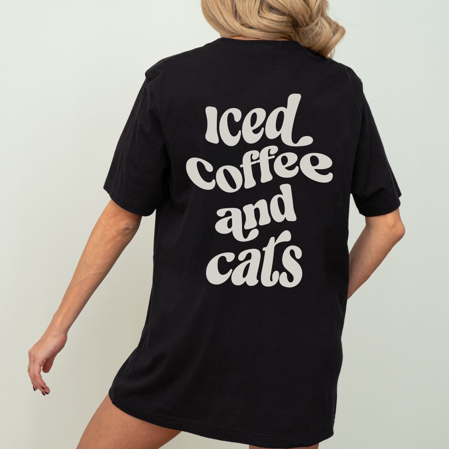 T-shirt with “Iced Coffee and Cats” in bold lettering, modeled in a cozy indoor setting.