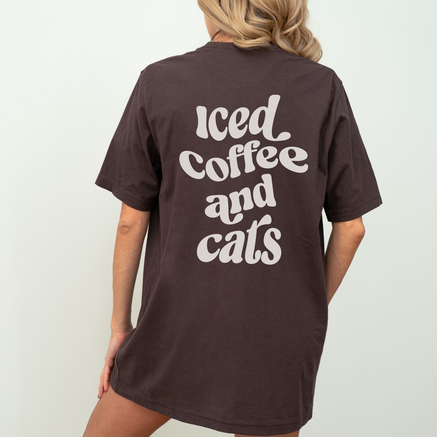 T-shirt with “Iced Coffee and Cats” in bold lettering, modeled in a cozy indoor setting.