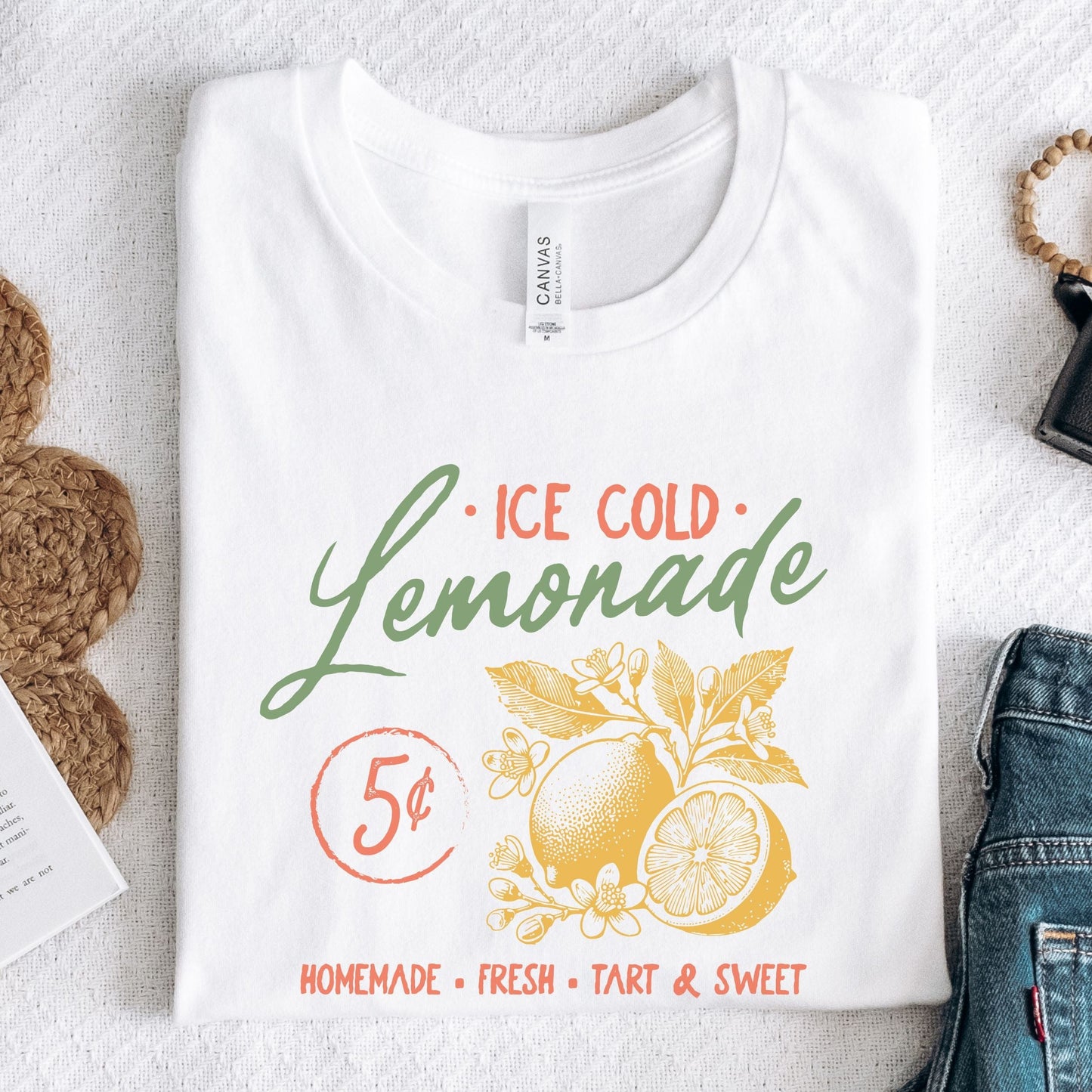 T-shirt design featuring vintage-style "Ice Cold Lemonade" text with yellow lemons, floral details, and a 5¢ sign for a retro summer vibe.