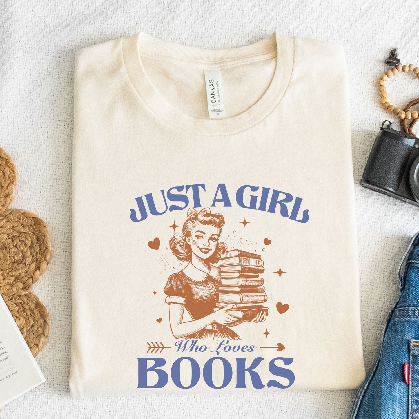 Vintage-style graphic tee that says "Just a Girl Who Loves Books" with a retro girl holding a stack of books and heart accents.