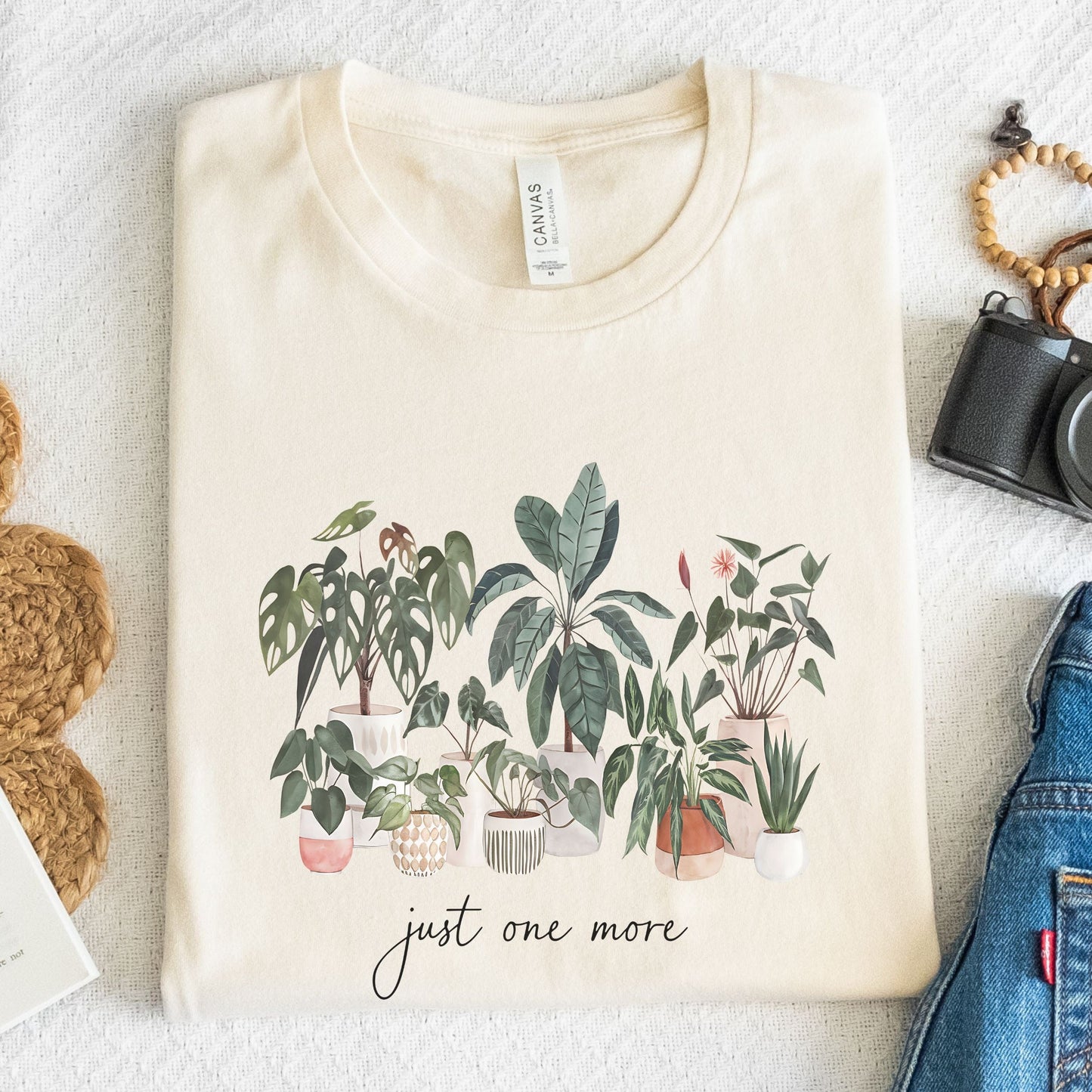 T-shirt with potted houseplants in watercolor style — monstera, rubber plant, snake plant, and more on a black background.