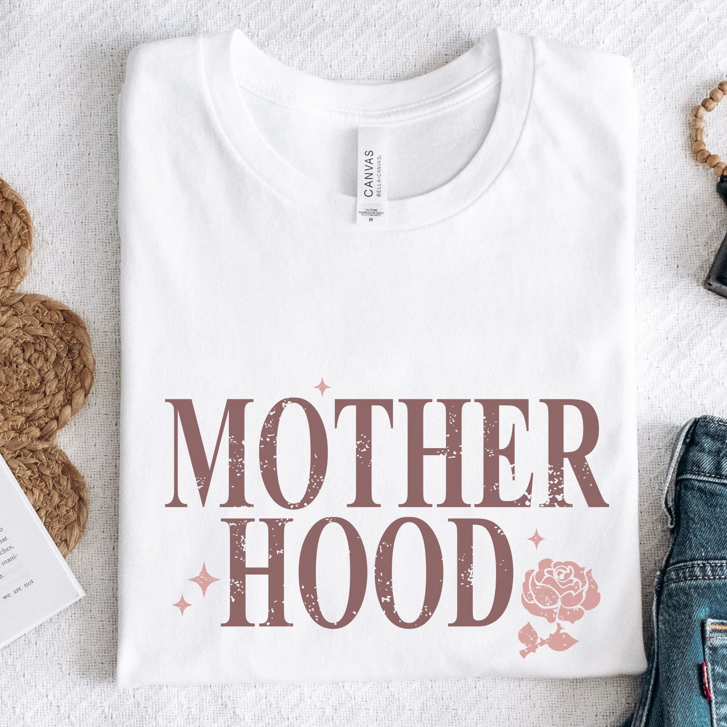 T-shirt with “Motherhood” text in distressed font and floral graphic. A soft, meaningful gift tee for moms.