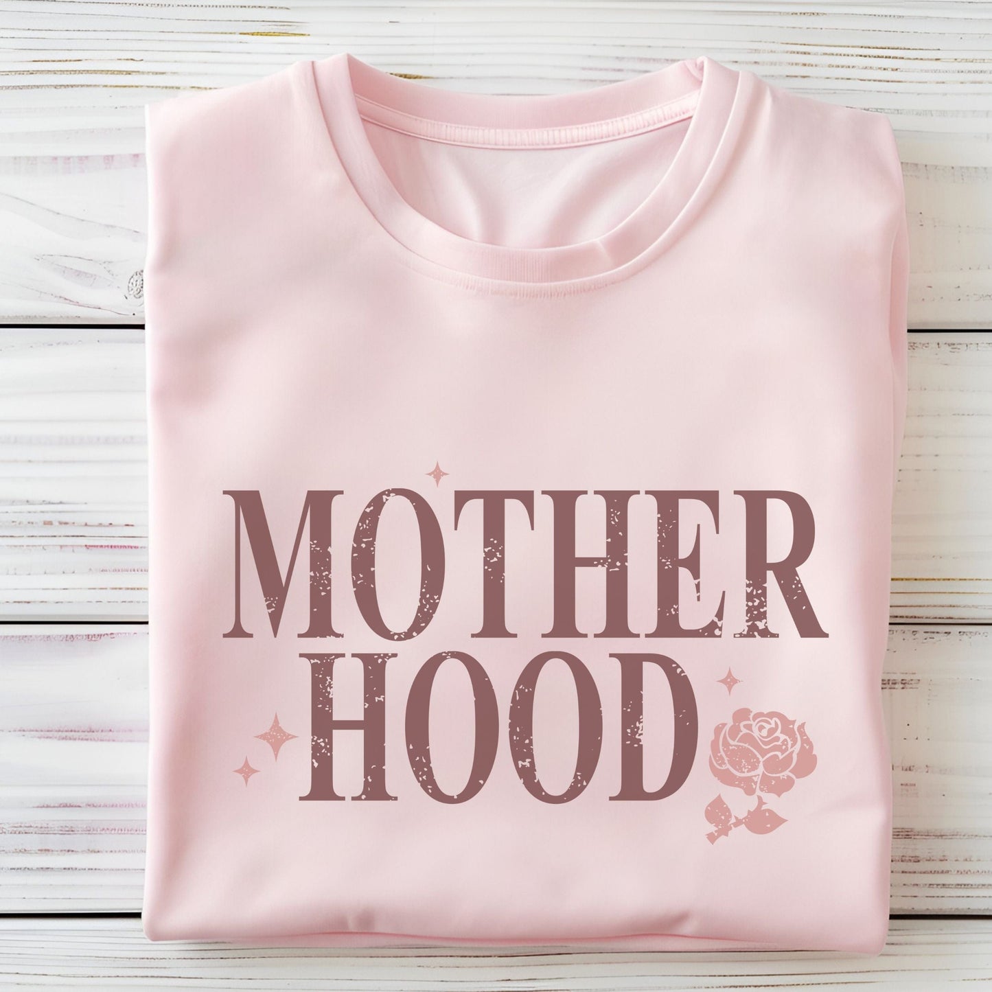T-shirt with “Motherhood” text in distressed font and floral graphic. A soft, meaningful gift tee for moms.