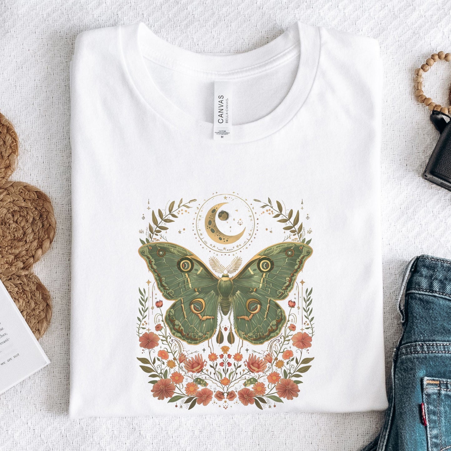 T-shirt design featuring a green luna moth with moon and stars above, surrounded by whimsical flowers and botanical elements in a cottagecore style