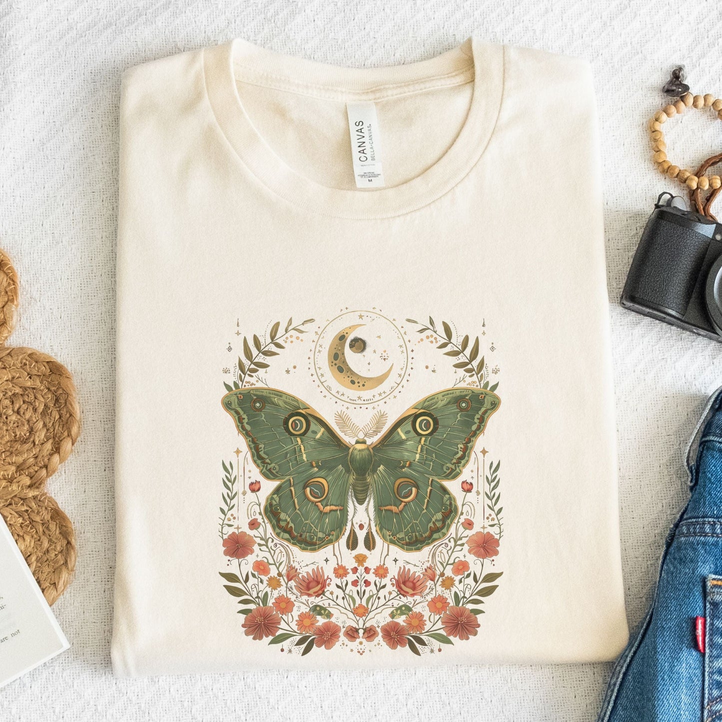 T-shirt design featuring a green luna moth with moon and stars above, surrounded by whimsical flowers and botanical elements in a cottagecore style