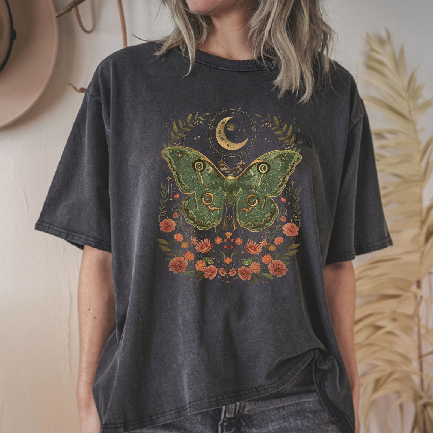 T-shirt design featuring a green luna moth with moon and stars above, surrounded by whimsical flowers and botanical elements in a cottagecore style