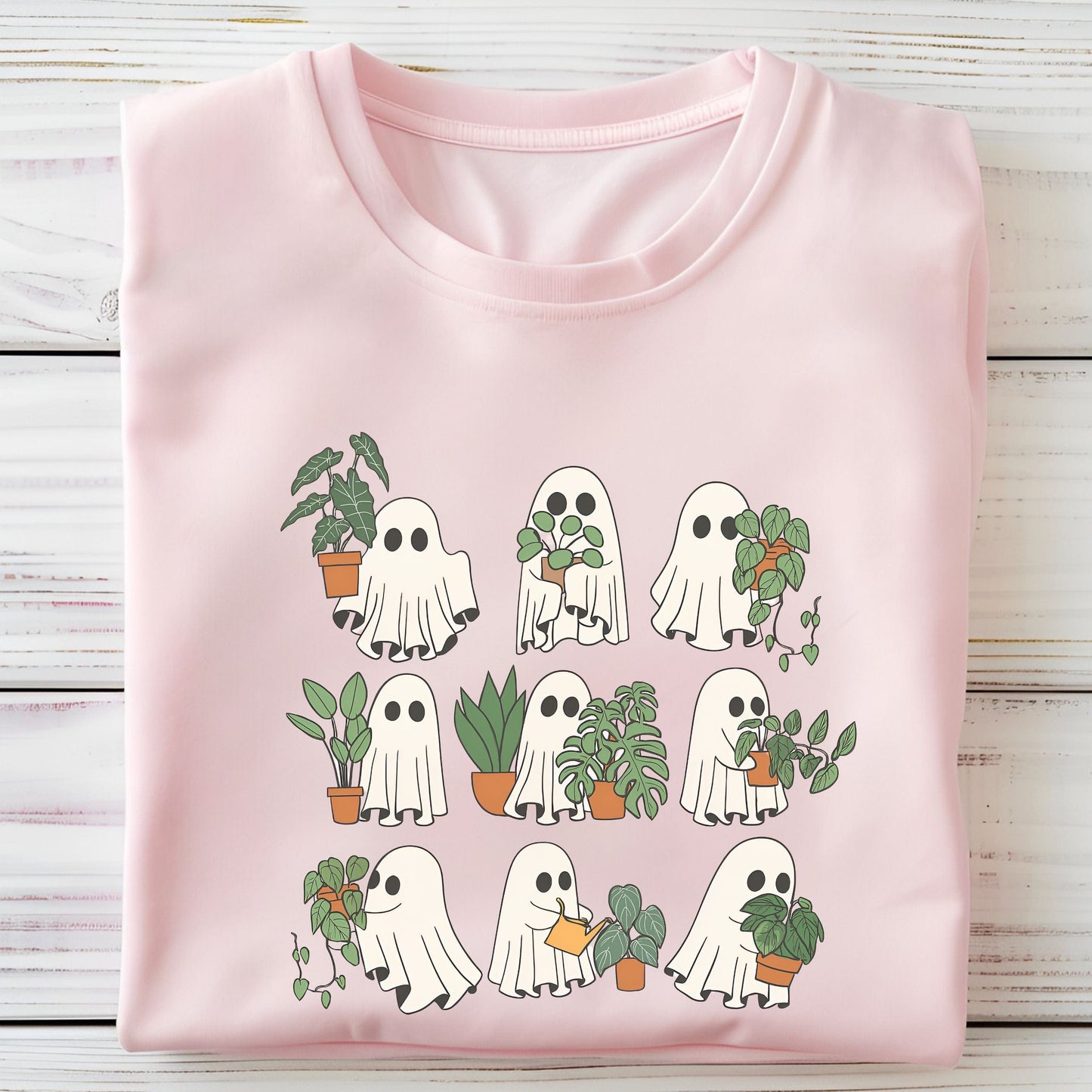 Pink t-shirt with ghost and plant design on a wooden surface