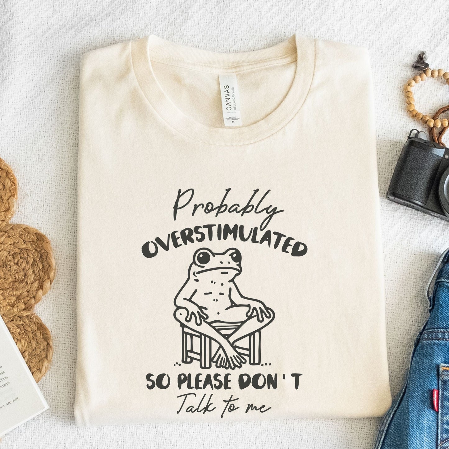 T-shirt with a cute frog illustration and "Probably Overstimulated" quote in hand-drawn font in natural
