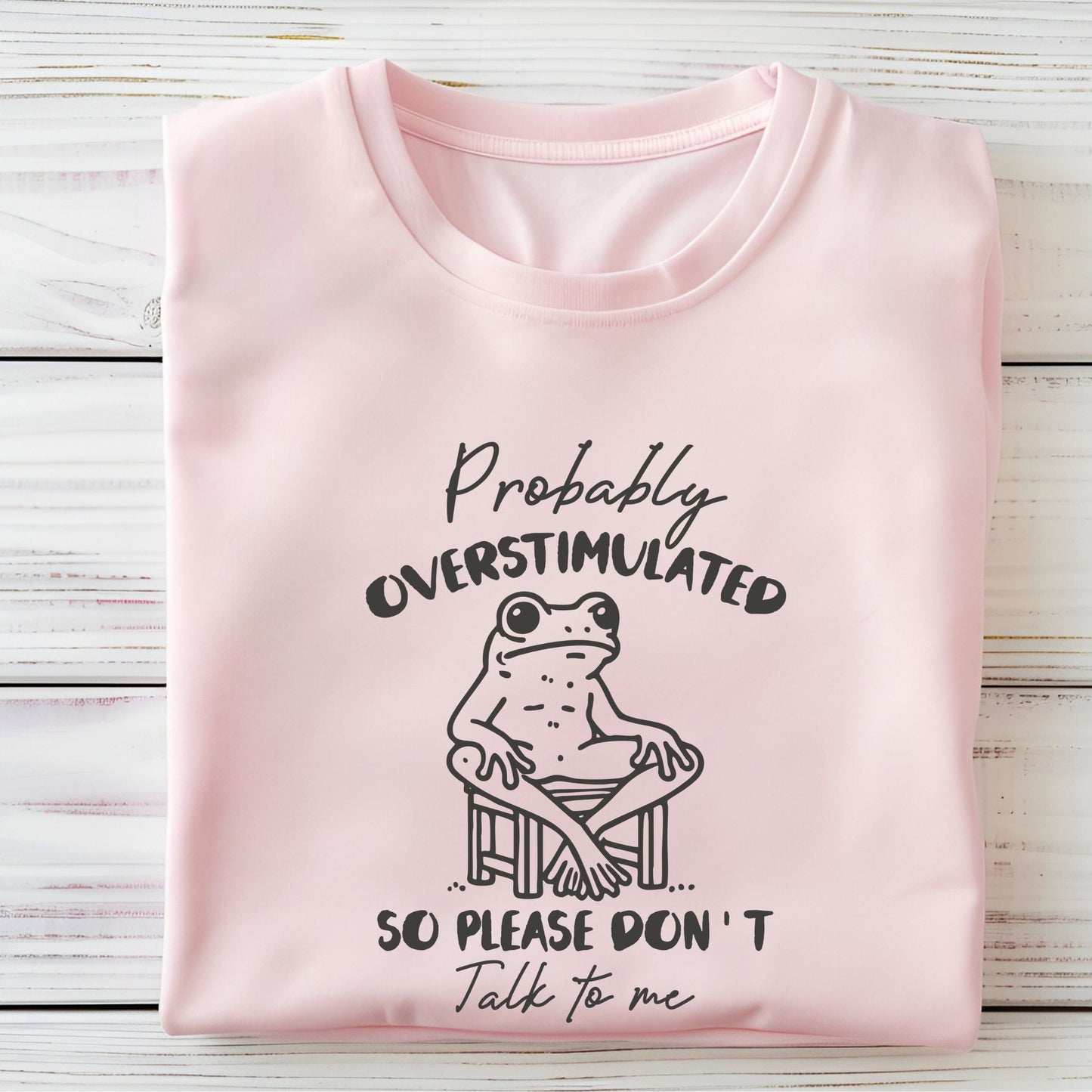 T-shirt with a cute frog illustration and "Probably Overstimulated" quote in hand-drawn font in soft pink