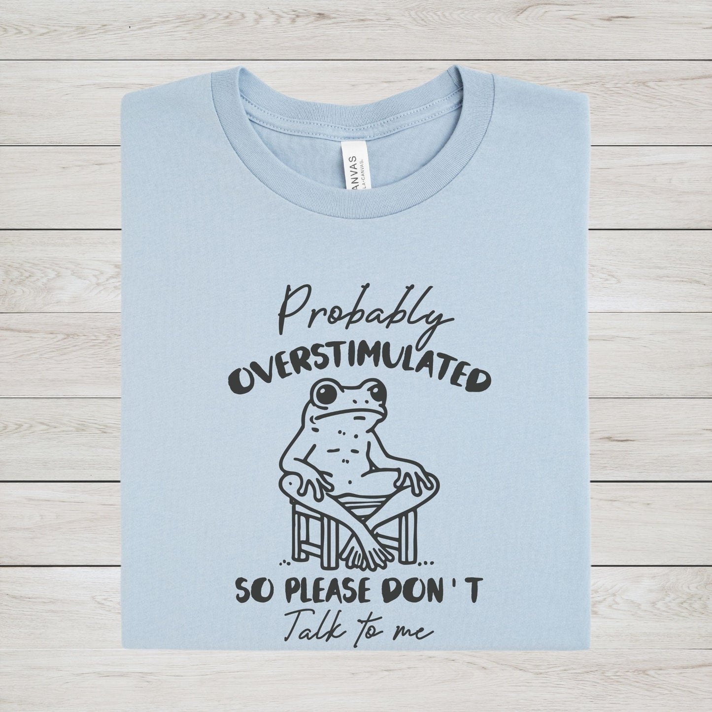 T-shirt with a cute frog illustration and "Probably Overstimulated" quote in hand-drawn font n light blue