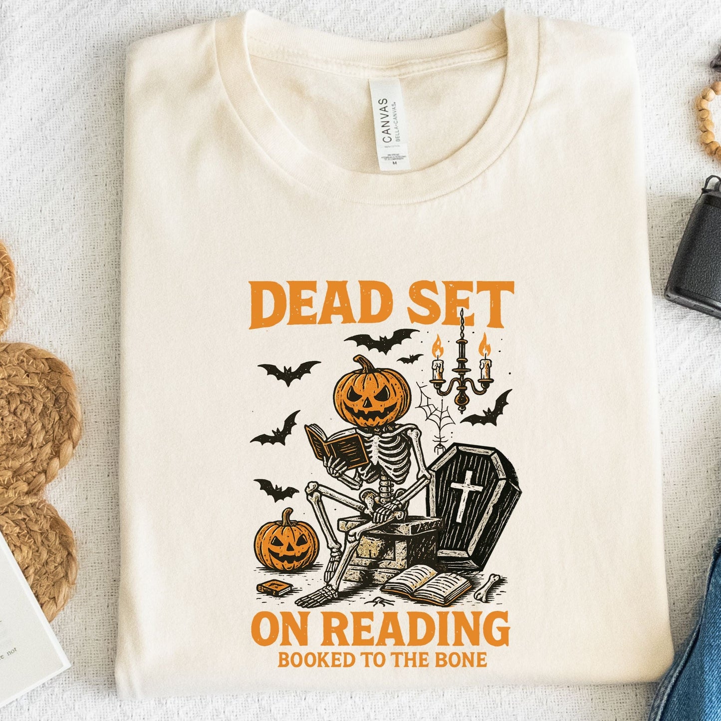 Vintage Halloween t-shirt with a skeleton reading a book, pumpkin head, bats, and spooky autumn vibe