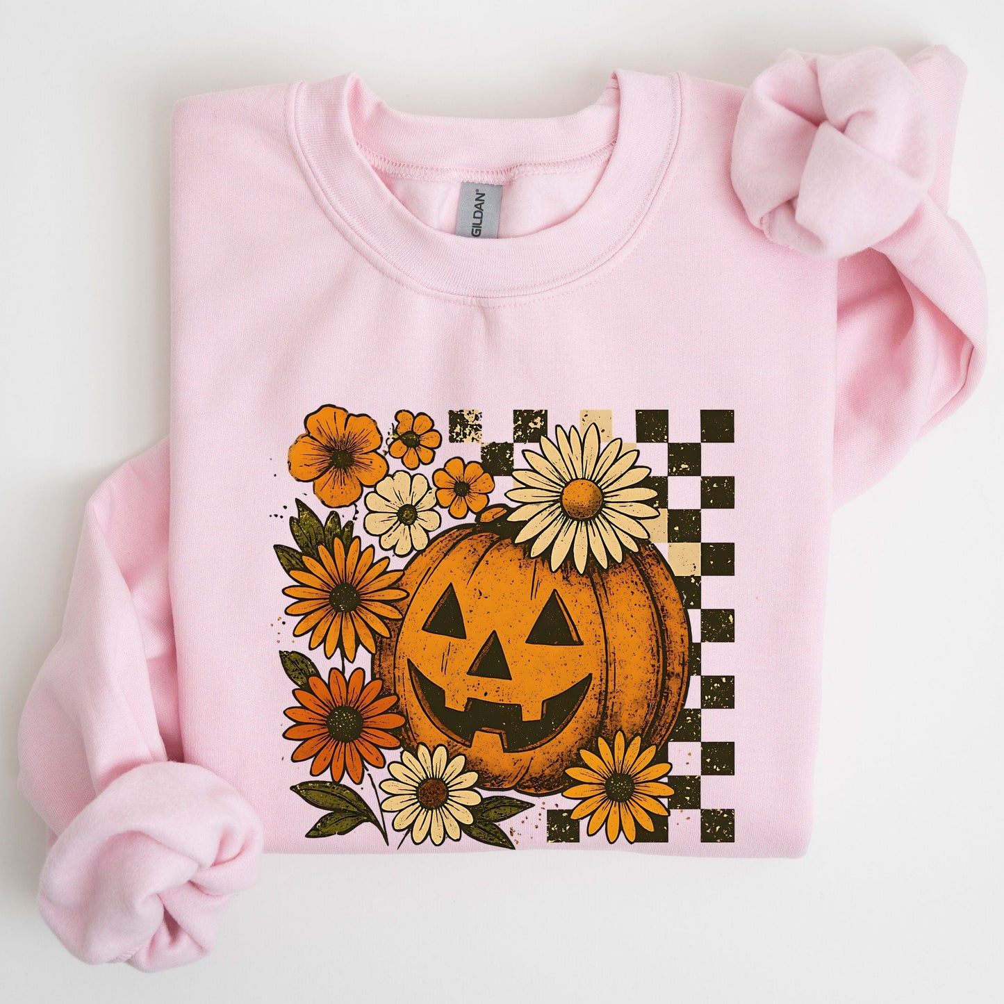 Pink sweatshirt with a Halloween-themed design featuring a pumpkin and flowers on a white background.