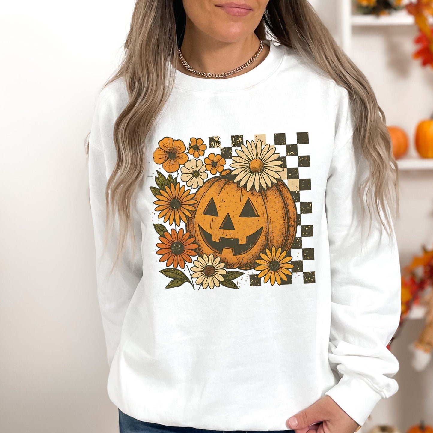 White sweatshirt with a pumpkin and floral design worn by a person.