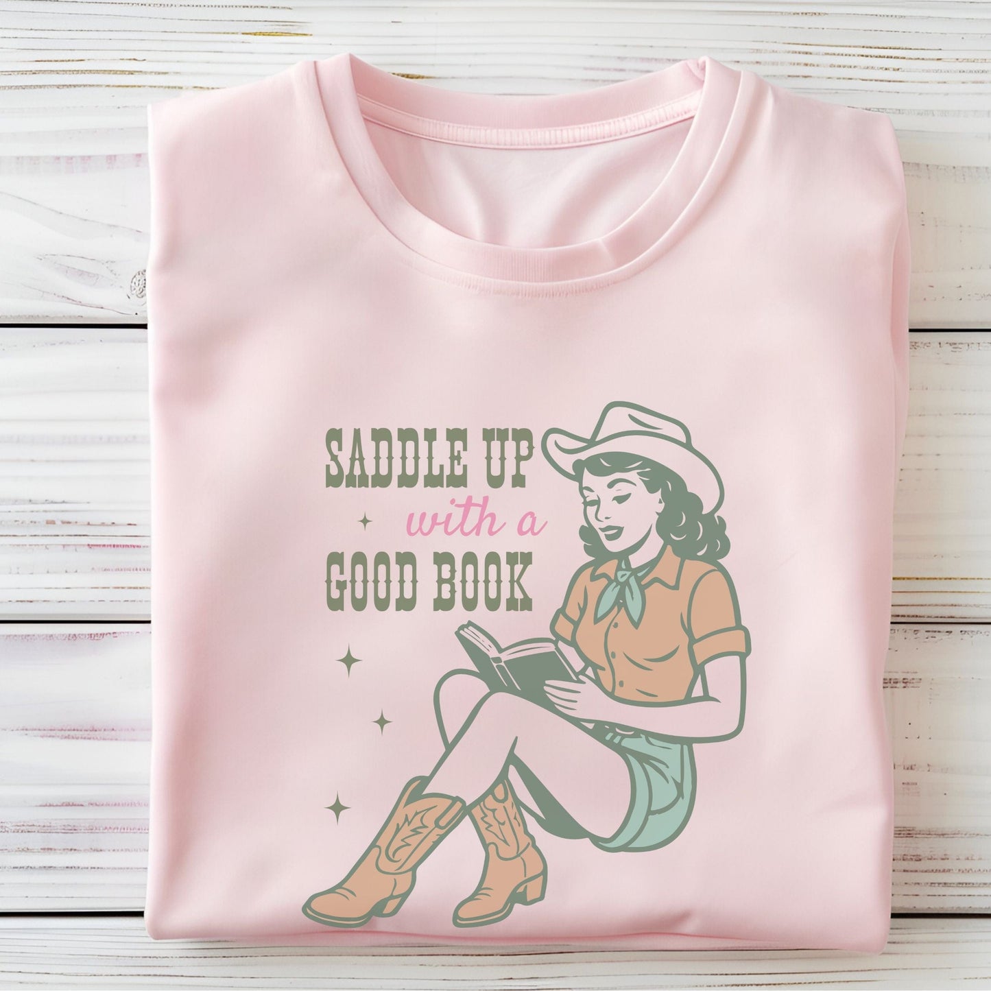 Folded t-shirt with Saddle Up With A Good Book design in soft pink