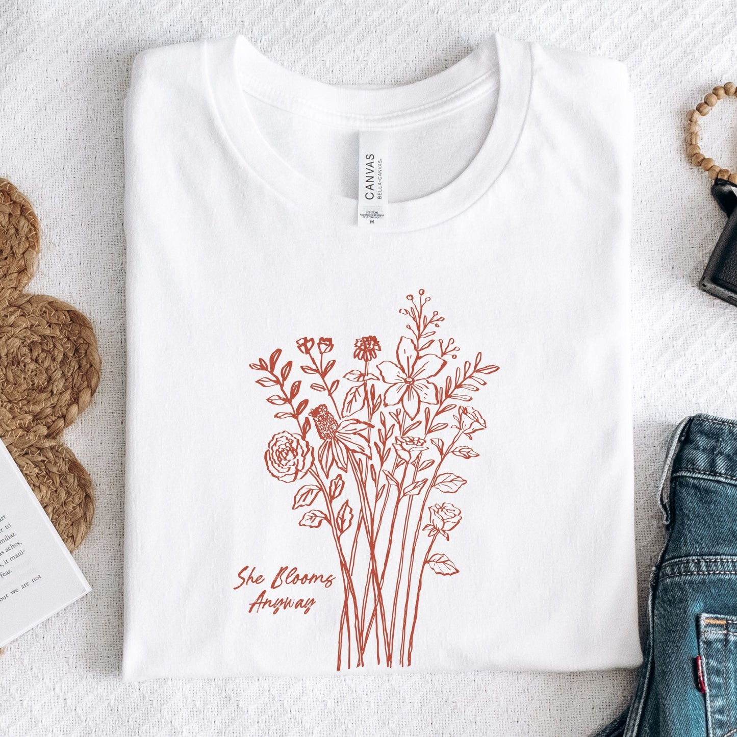 Floral graphic t-shirt with hand-drawn wildflowers and the quote “She Blooms Anyway”