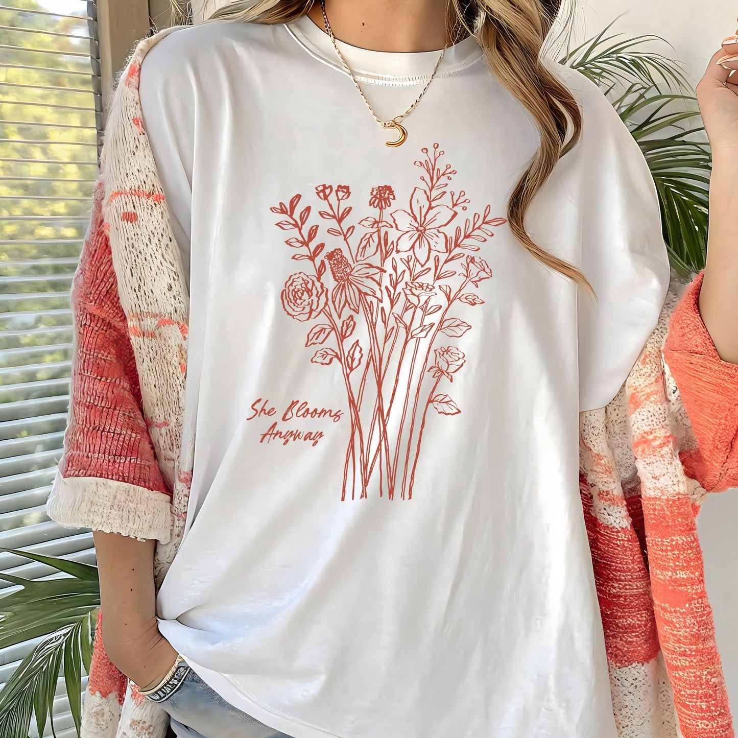 Floral graphic t-shirt with hand-drawn wildflowers and the quote “She Blooms Anyway”