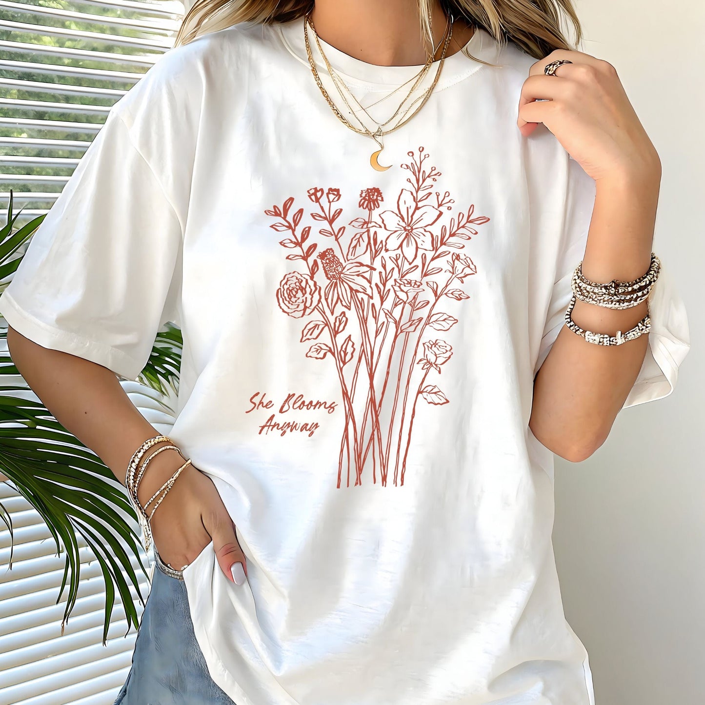 Floral graphic t-shirt with hand-drawn wildflowers and the quote “She Blooms Anyway”