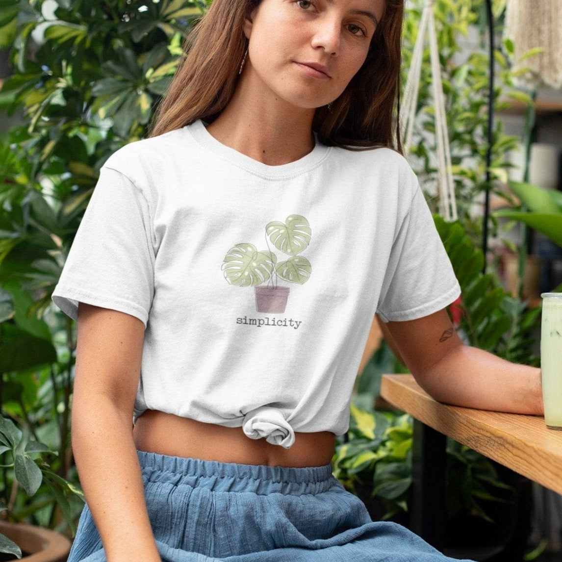 “Simplicity” t-shirt with minimalist monstera plant in a muted pink pot and soft, modern lettering beneath the design.
