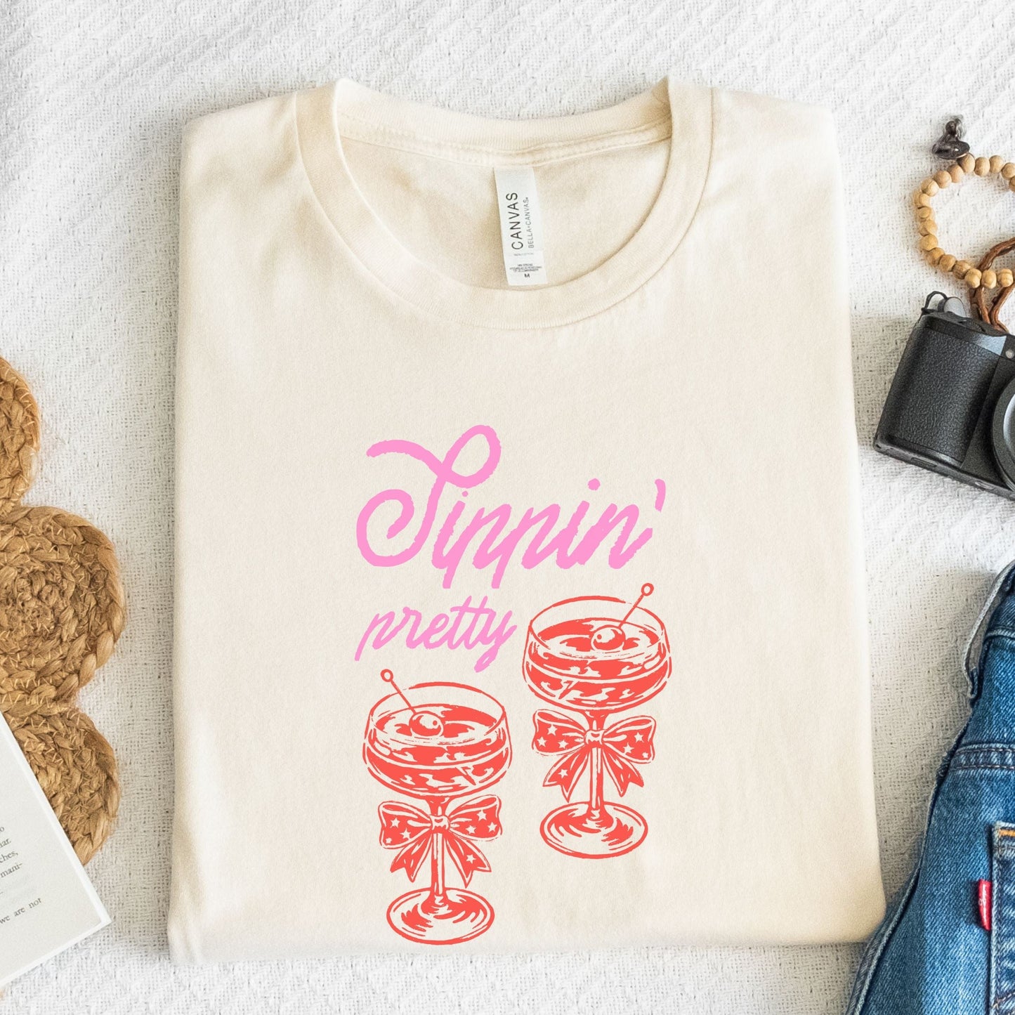 Vintage style t-shirt with “Sippin' Pretty” text and two illustrated coupe cocktail glasses with bows