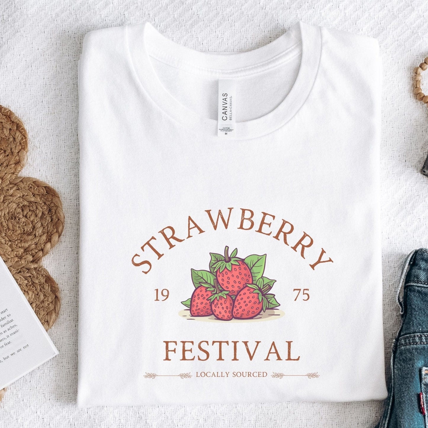 “Strawberry Festival” t-shirt with a vintage berry illustration, arched retro text, and “locally sourced” detail in rustic tones.