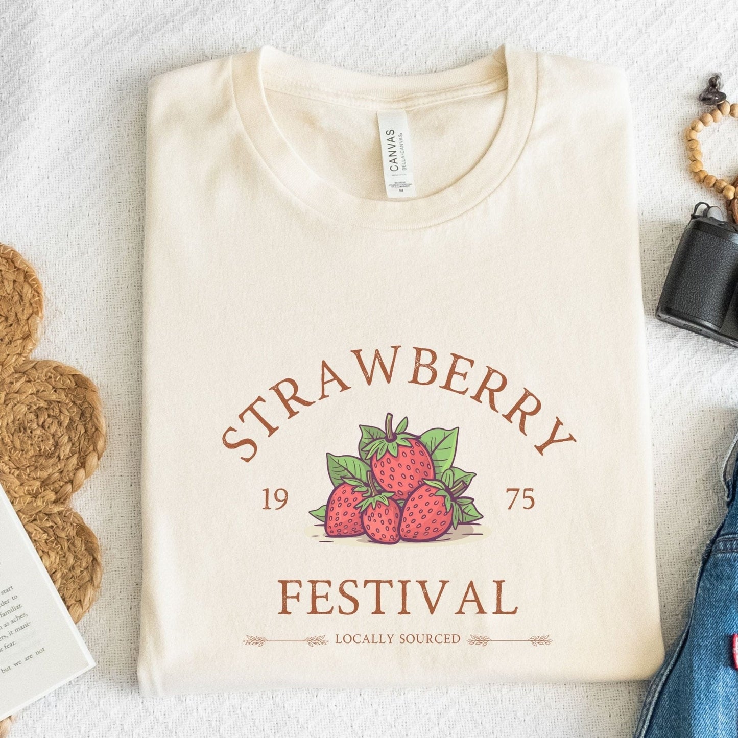 “Strawberry Festival” t-shirt with a vintage berry illustration, arched retro text, and “locally sourced” detail in rustic tones.