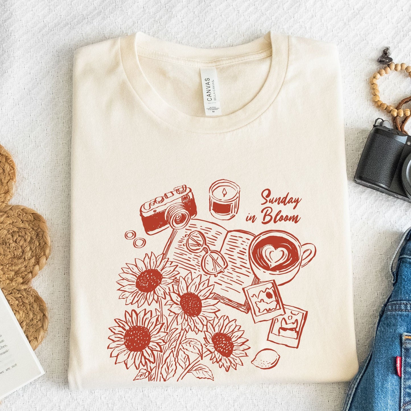 T-shirt with 'Sunday in Bloom' design featuring coffee, book, flowers, and vintage camera in natural