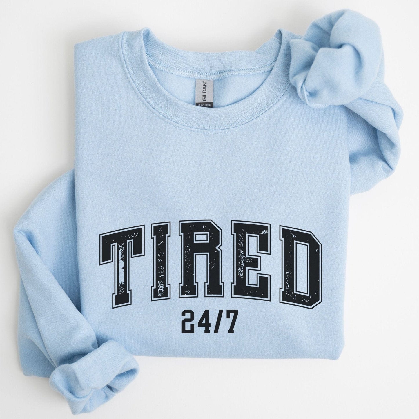 “Tired 24/7” sweatshirt with varsity block letters and a distressed texture — cozy and relatable for the chronically exhausted.