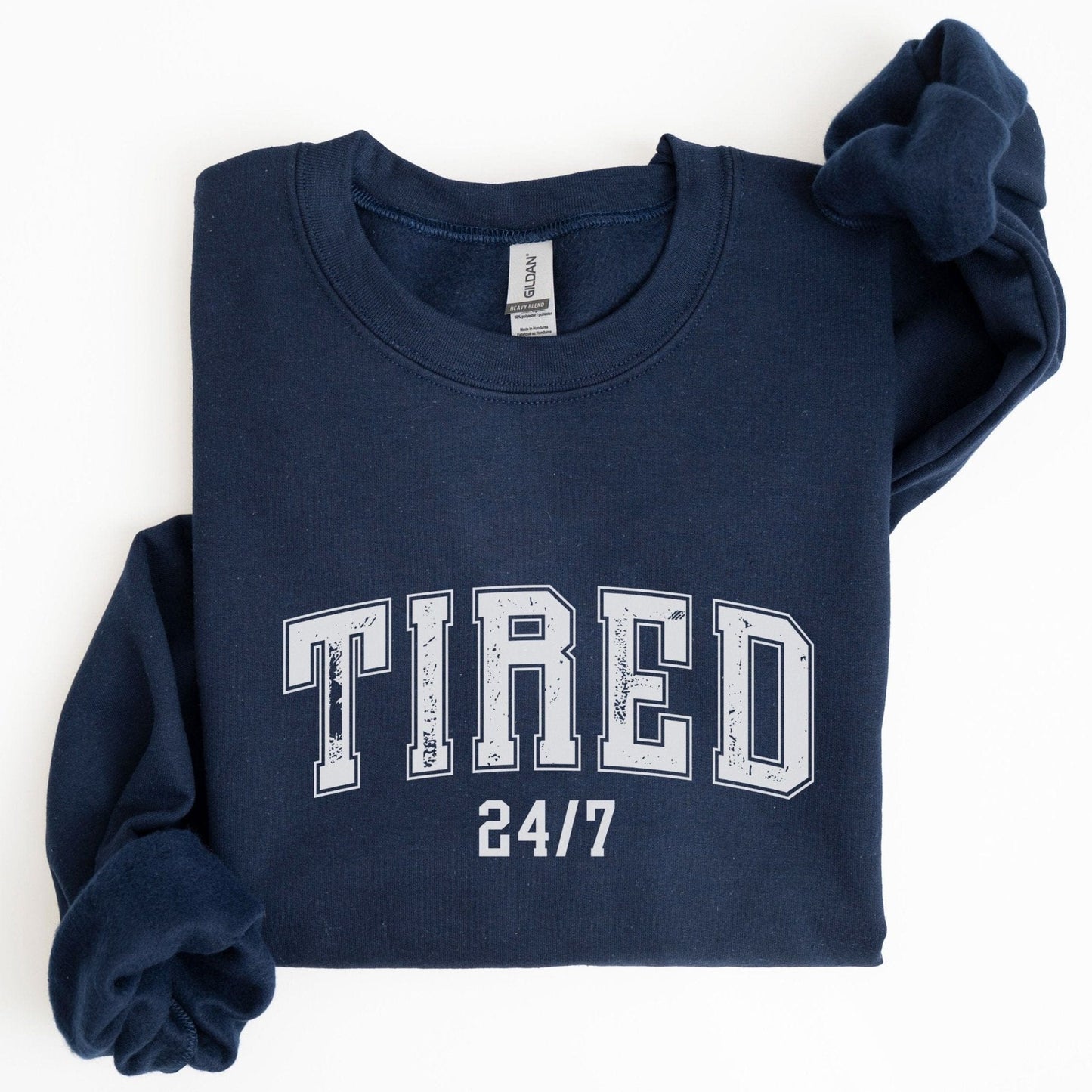 “Tired 24/7” sweatshirt with varsity block letters and a distressed texture — cozy and relatable for the chronically exhausted.