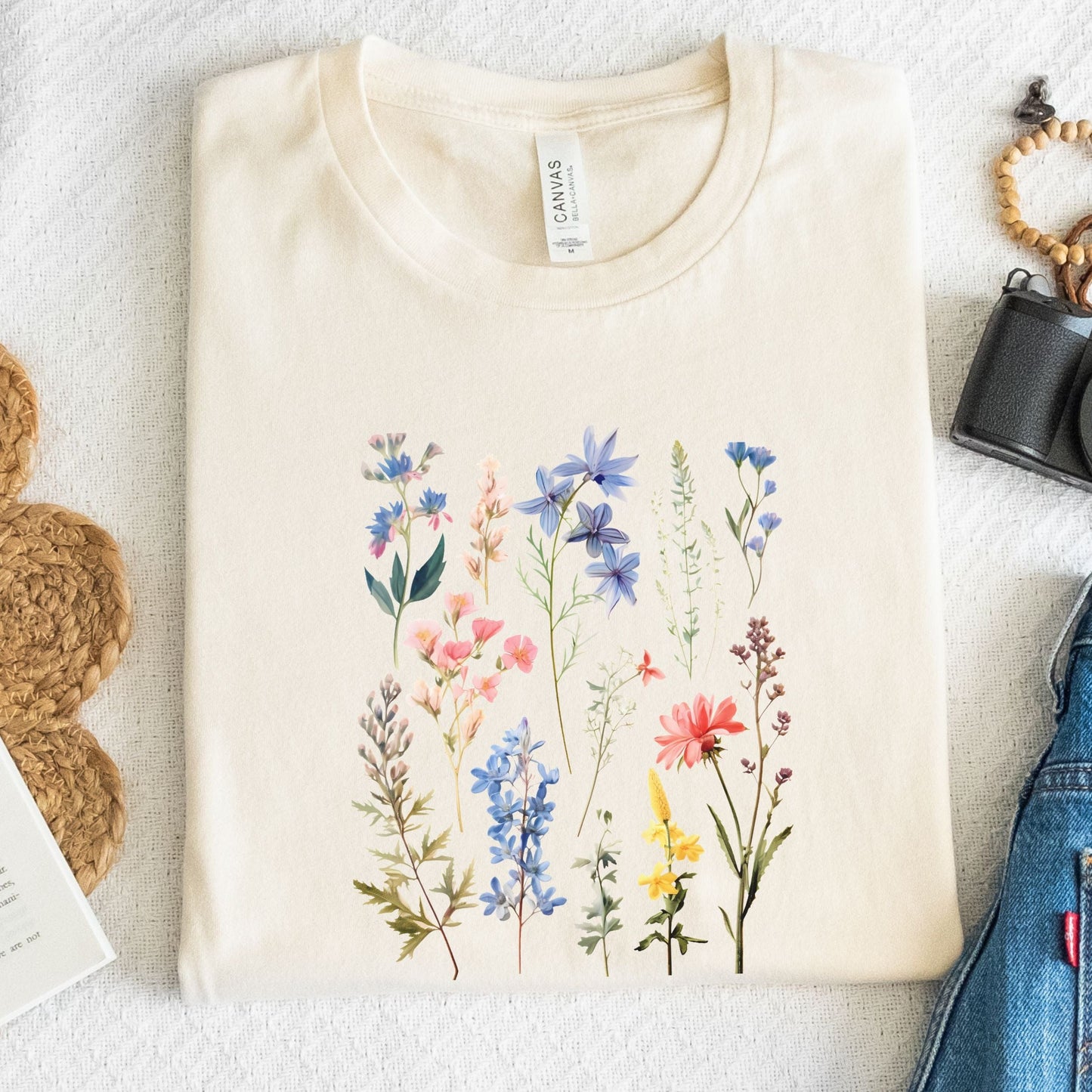 Vintage wildflower t-shirt featuring hand-drawn pastel florals in soft pinks, blues, and yellows arranged in a scattered botanical layout.