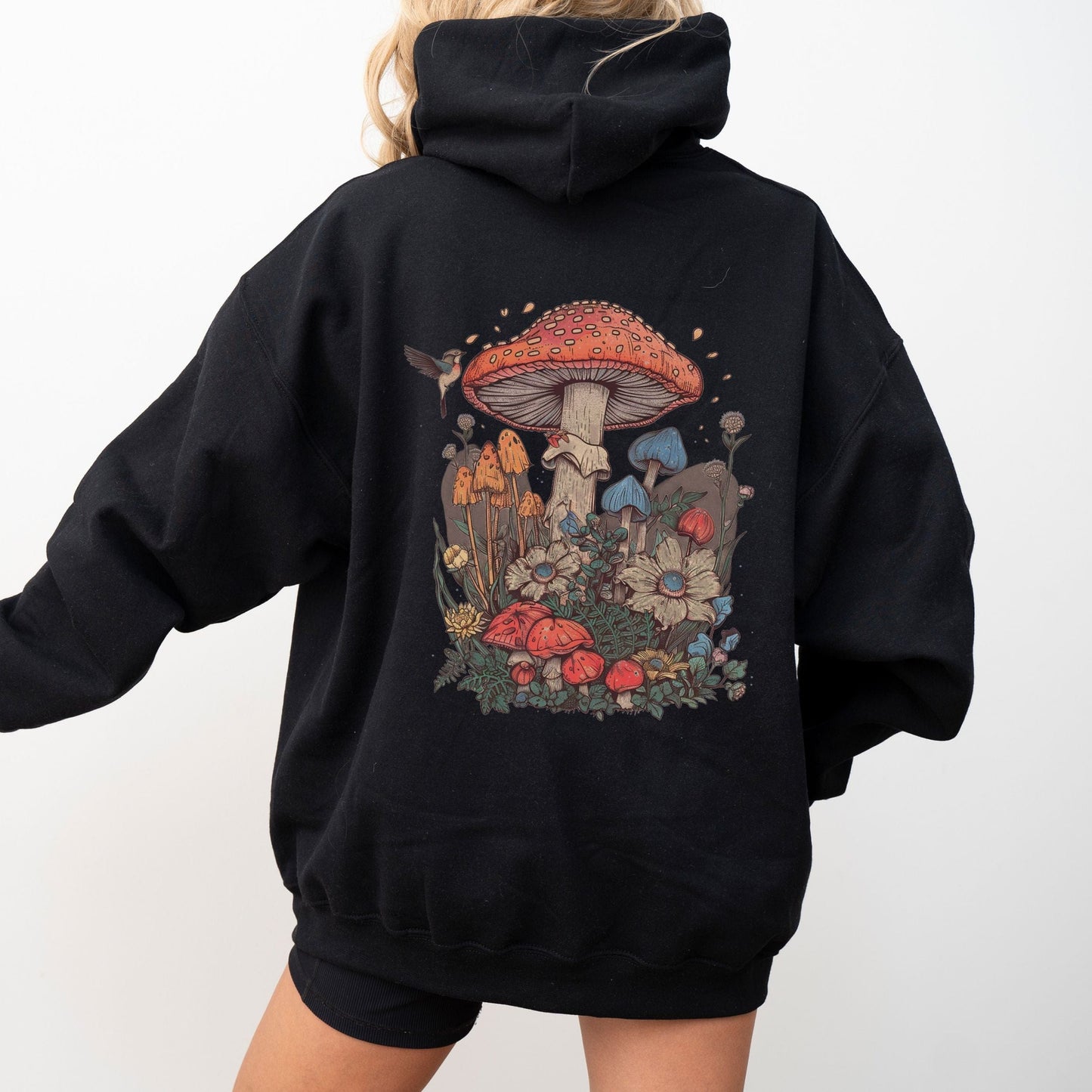 Back hoodie design featuring whimsical mushrooms, wildflowers, and a hummingbird in a cottagecore spring forest setting