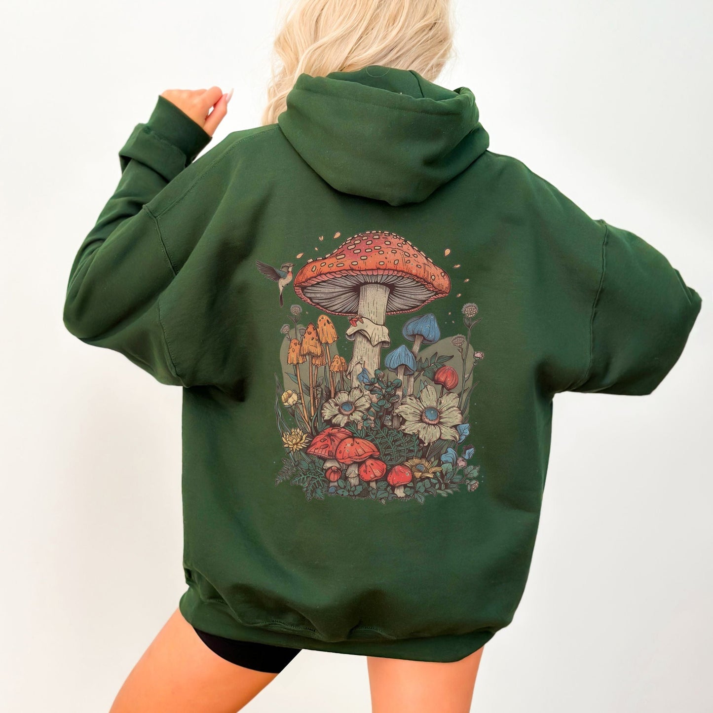 Back hoodie design featuring whimsical mushrooms, wildflowers, and a hummingbird in a cottagecore spring forest setting