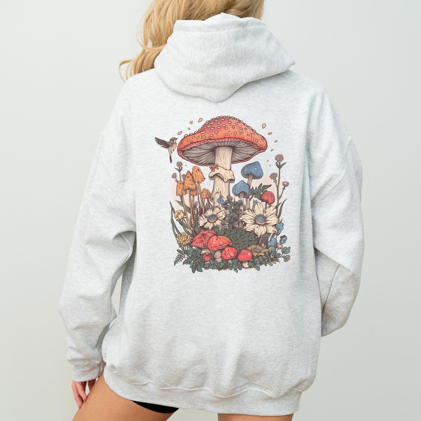 Back hoodie design featuring whimsical mushrooms, wildflowers, and a hummingbird in a cottagecore spring forest setting