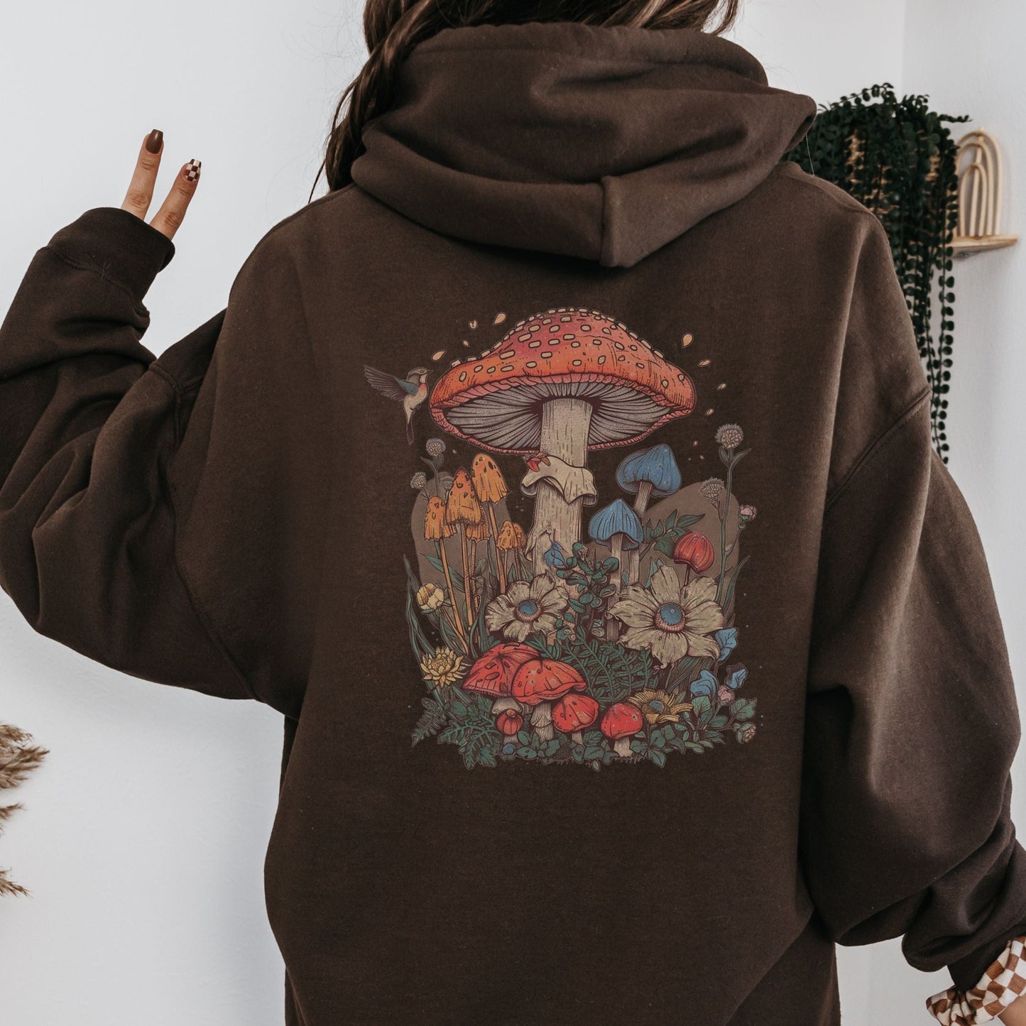 Back hoodie design featuring whimsical mushrooms, wildflowers, and a hummingbird in a cottagecore spring forest setting