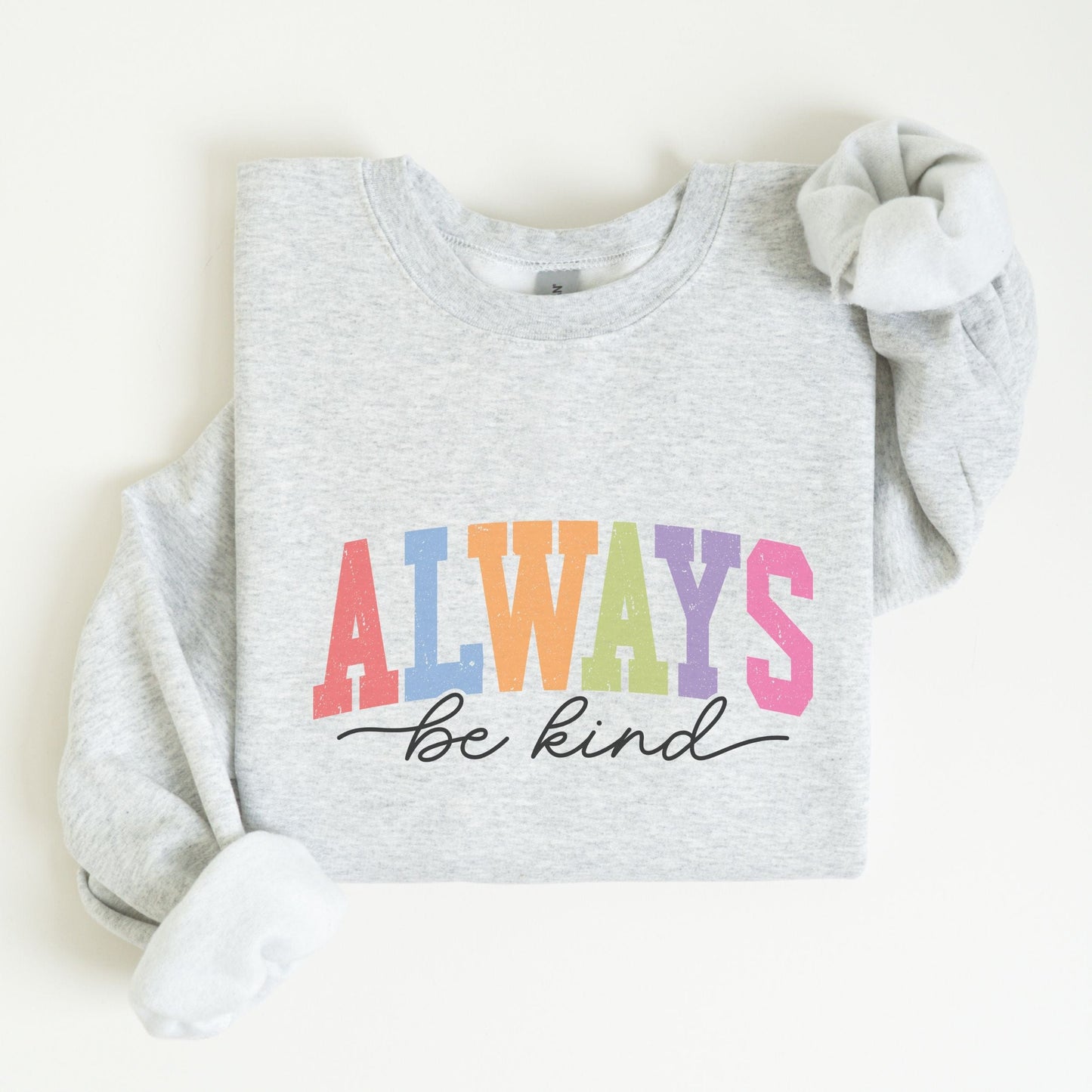 Retro rainbow “Always Be Kind” sweatshirt design with bold varsity letters in pastel colors and script font underneath on a cozy fleece pullover.