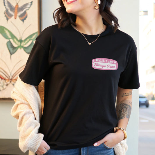 Pink and white name tag design that says “Hello I Am Always Tired,” printed on the left chest of a comfy t-shirt.