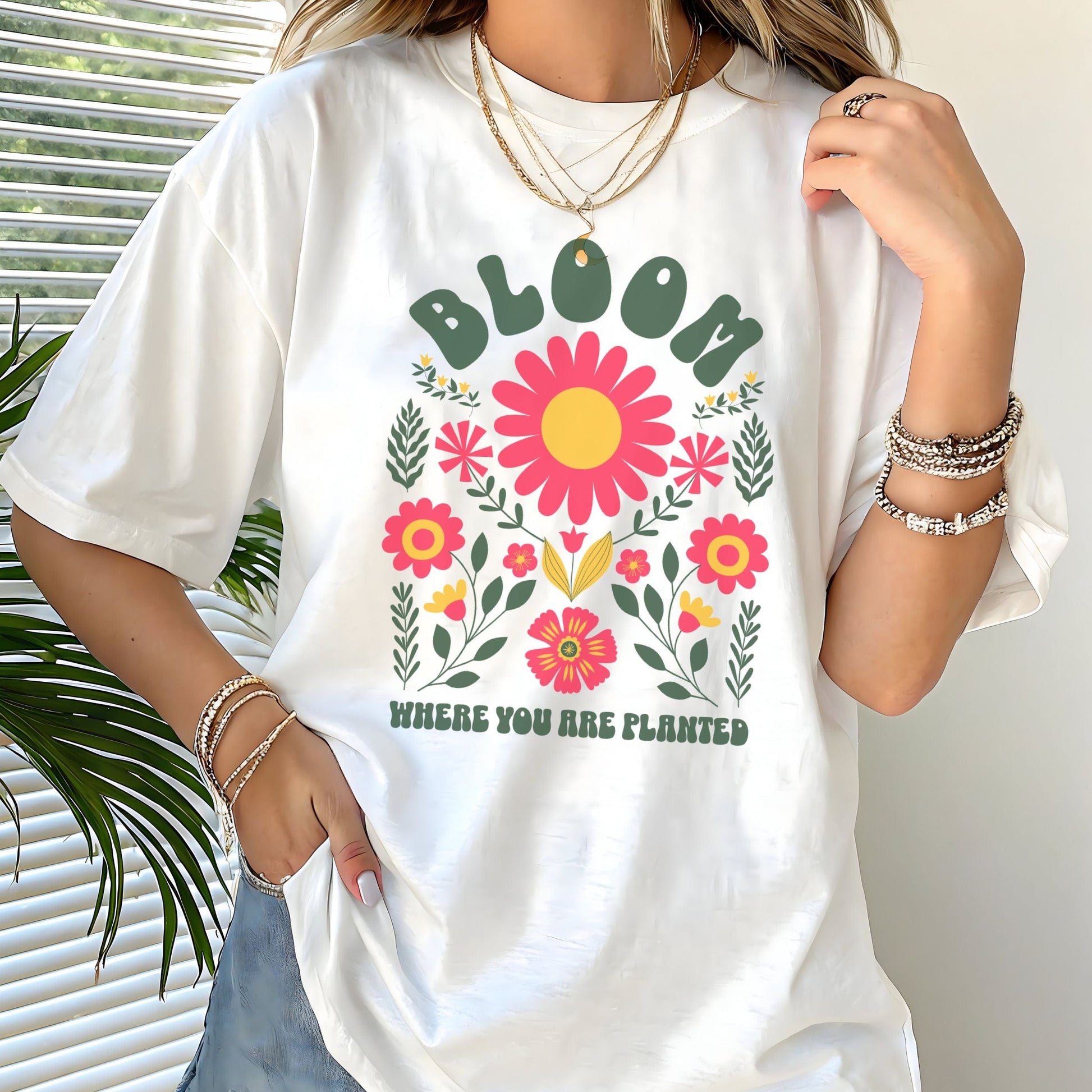 “Bloom Where You Are Planted” t-shirt with bold retro florals and uplifting message in green, pink, and yellow tones.
