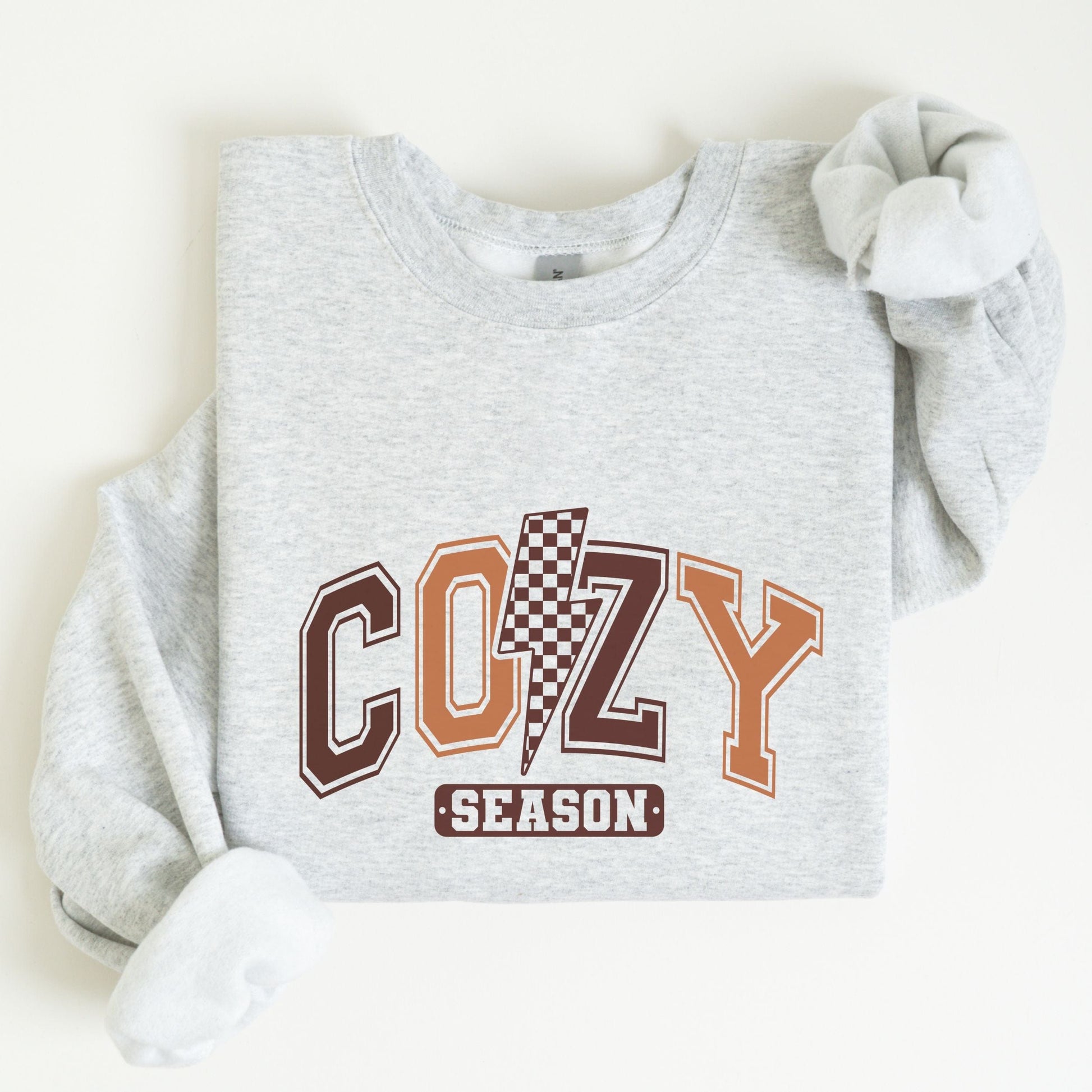 Cozy Season sweatshirt with retro varsity letters in fall colors and a checkered lightning bolt—perfect autumn apparel for cozy vibes.